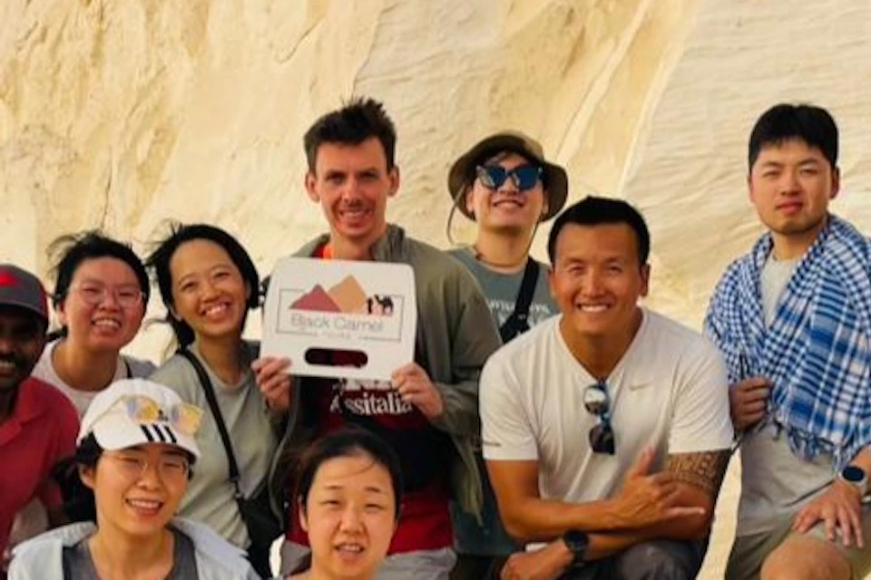 A group of people posing on a white rock formation under a clear blue sky, some wearing hats and sunglasses, smiling for the camera.