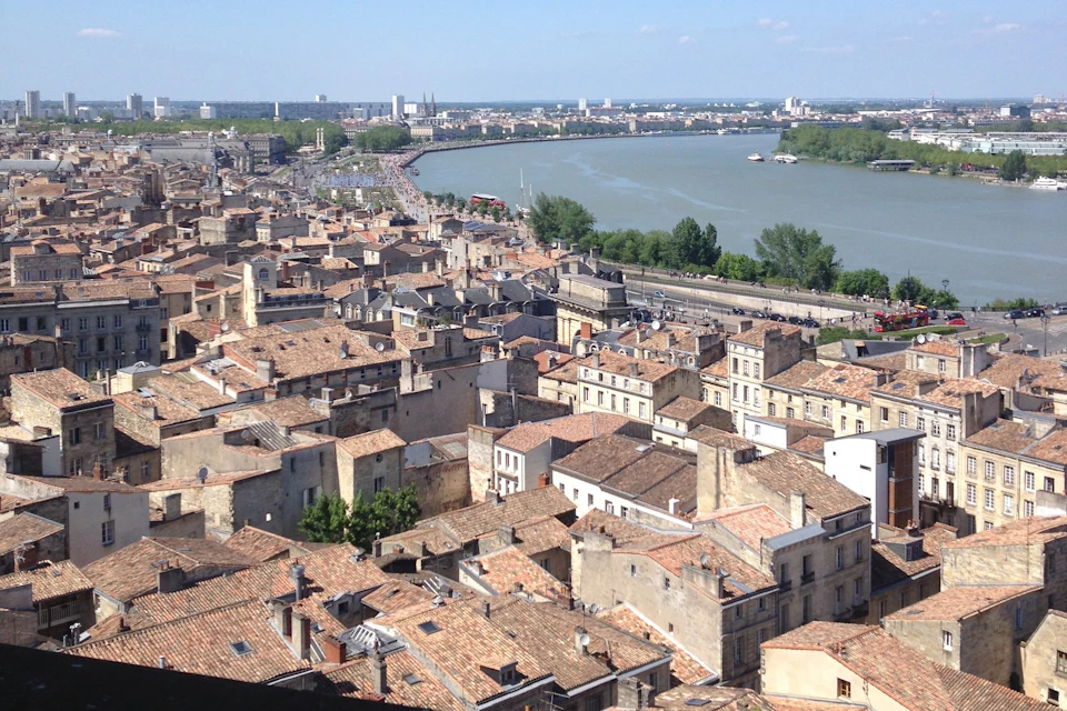 A cityscape with tiled rooftops, a river, and a distant horizon under a blue sky.