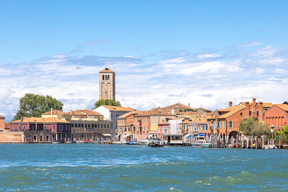A view of colorful buildings and a bell tower along a waterfront under a blue sky with clouds.