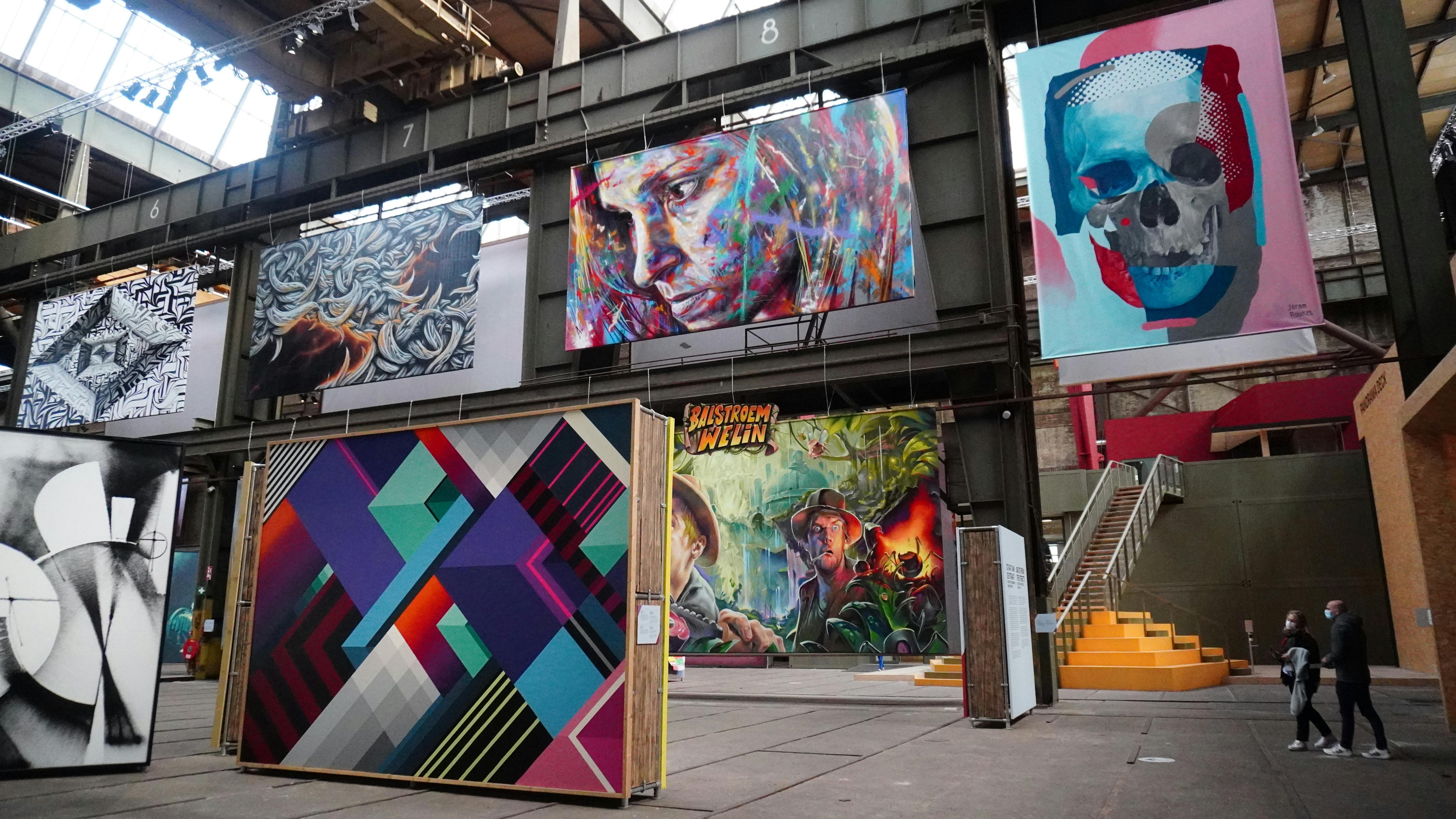 Velký sál s barevnými nástěnnými malbami na stěnách včetně abstraktních vzorů a portrétů. Vpravo jsou vidět schody.