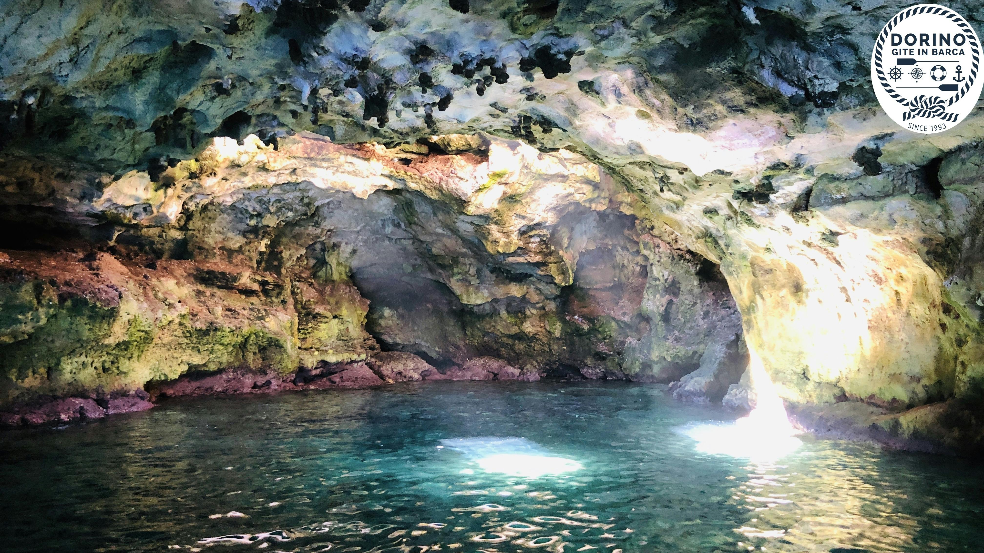 Interno di grotta illuminato dal sole con acqua turchese, pareti rocciose ricoperte di muschio e alghe e un'apertura naturale che lascia entrare la luce.