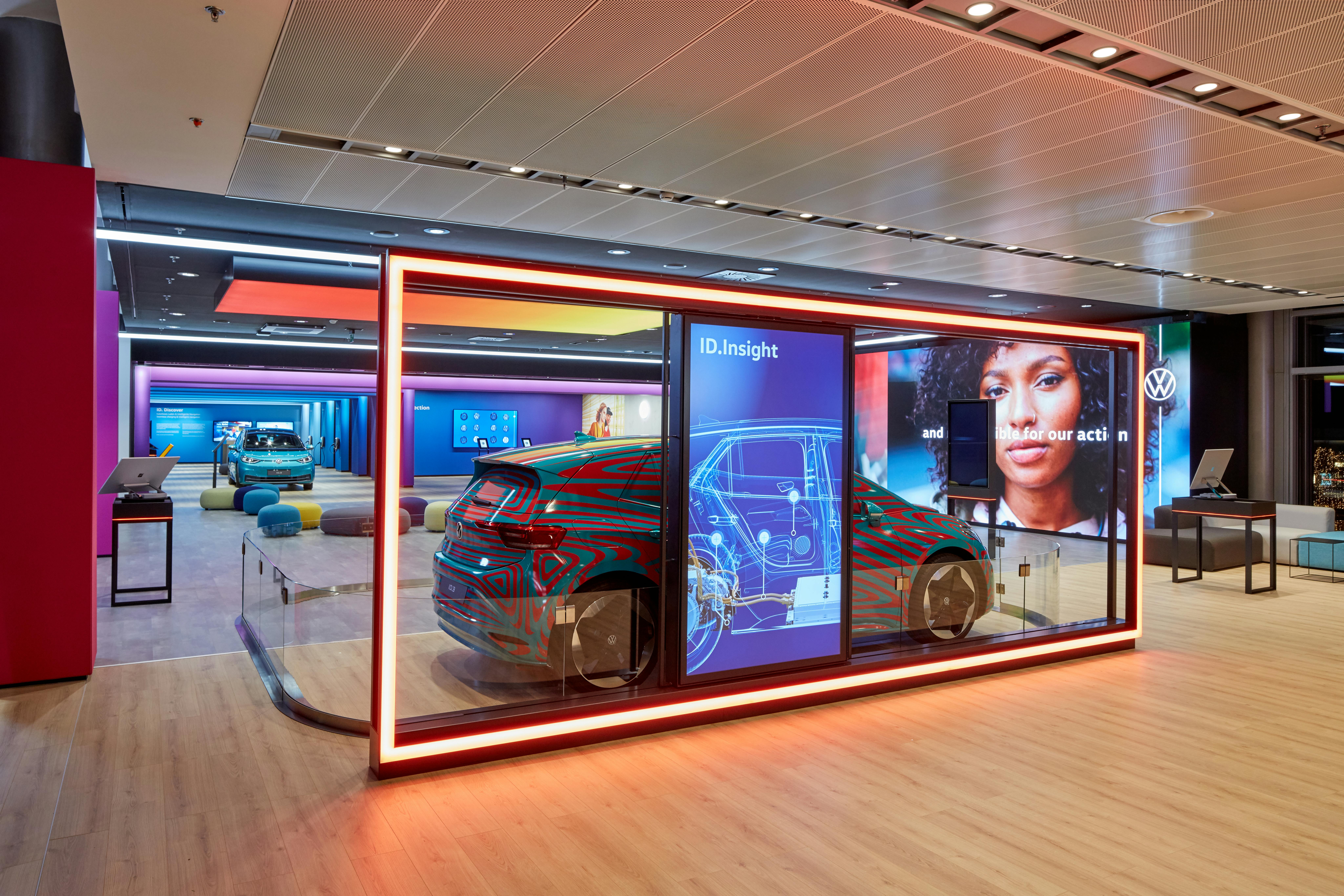 A modern showroom features a car display with technical schematics and a large screen showing a woman's face next to a Volkswagen logo.