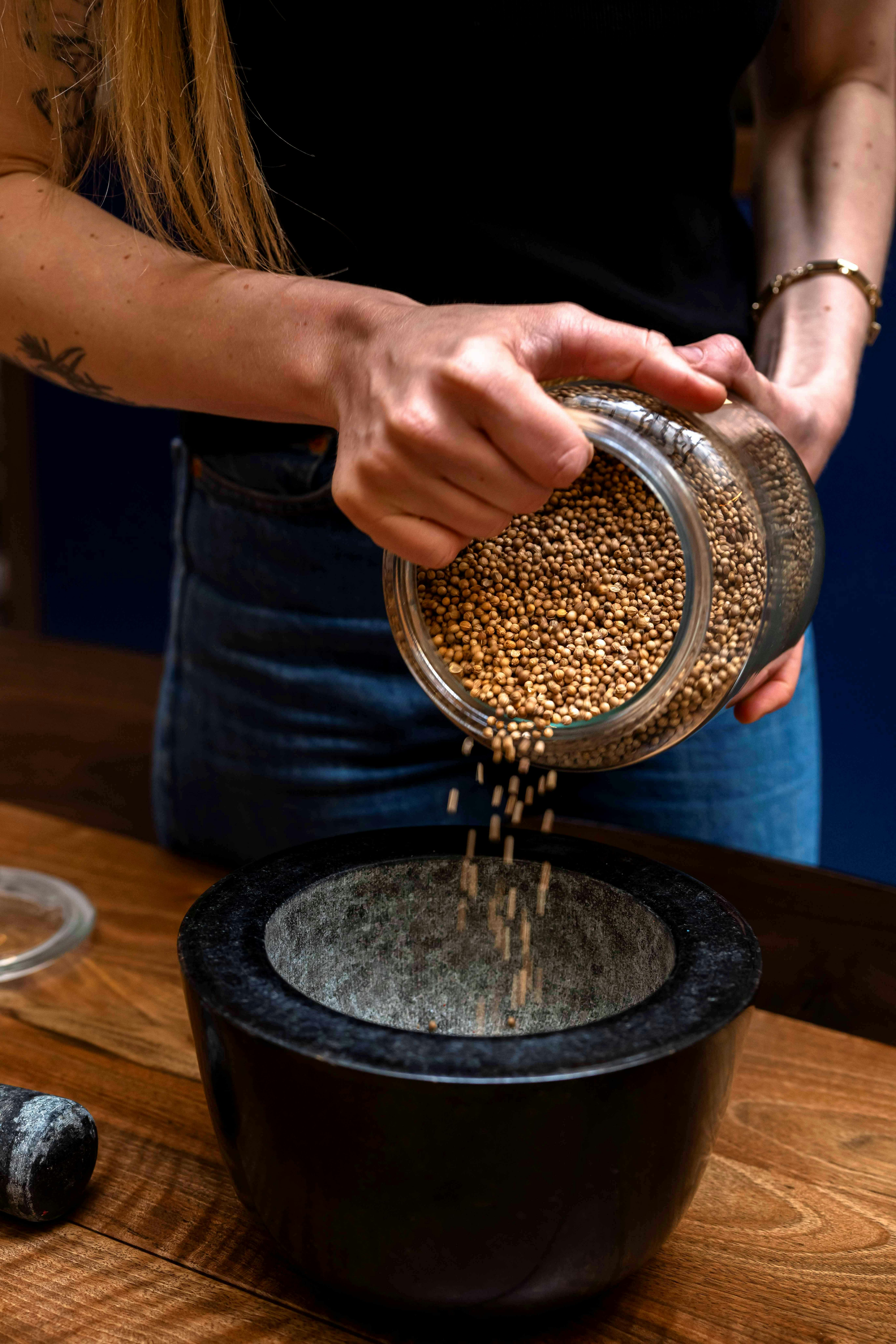 Человек, заливающий семена горчицы из банки в черный ступку на деревянном столе.