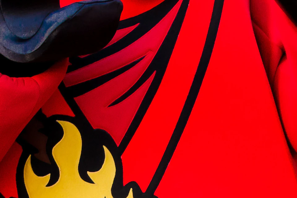 A person poses playfully with a large, red ninja LEGO character outside a themed building decorated with a dragon banner.