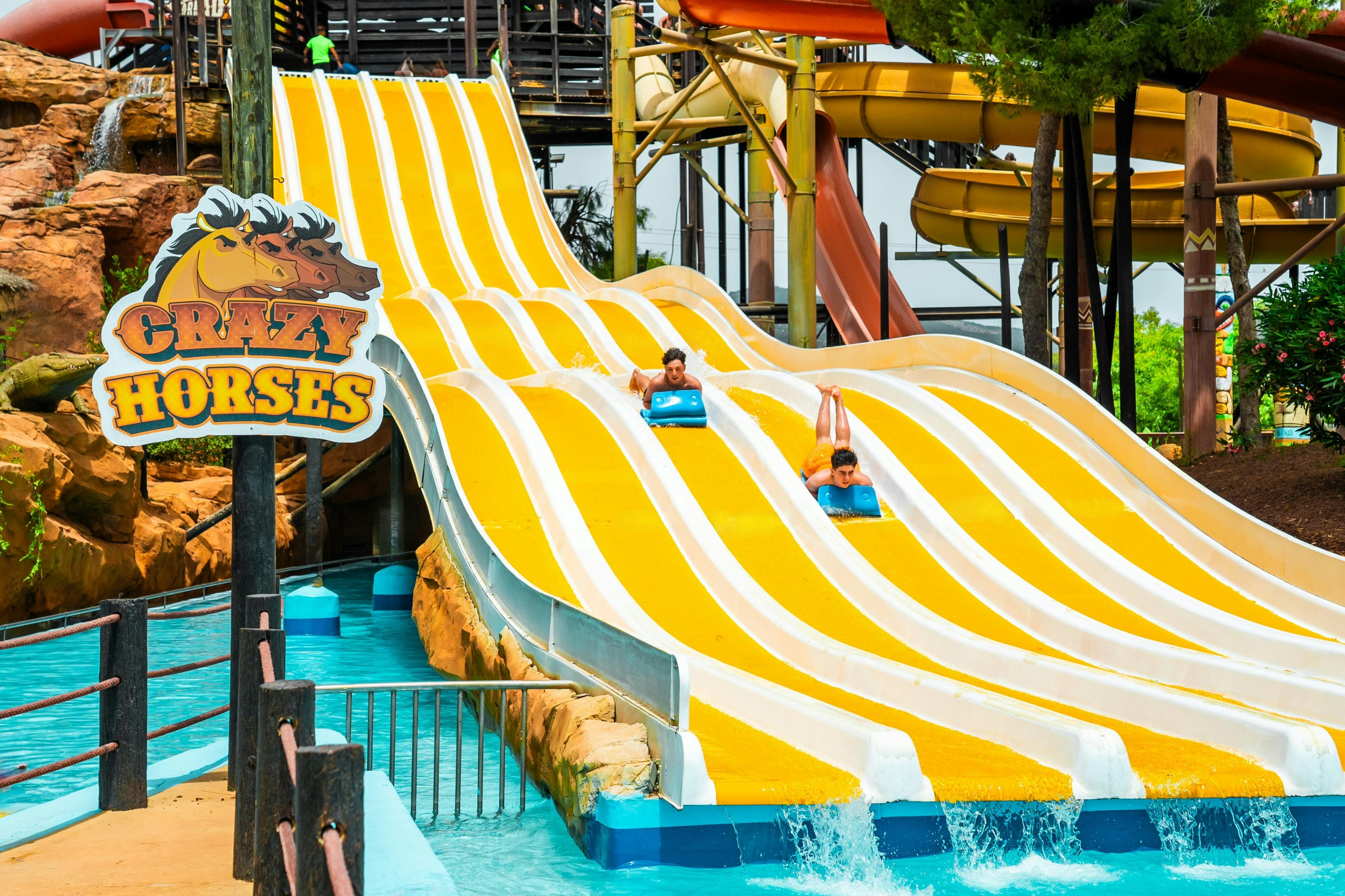 Twee mensen glijden van parallelle gele waterglijbanen op matten in een buitenwaterpark.