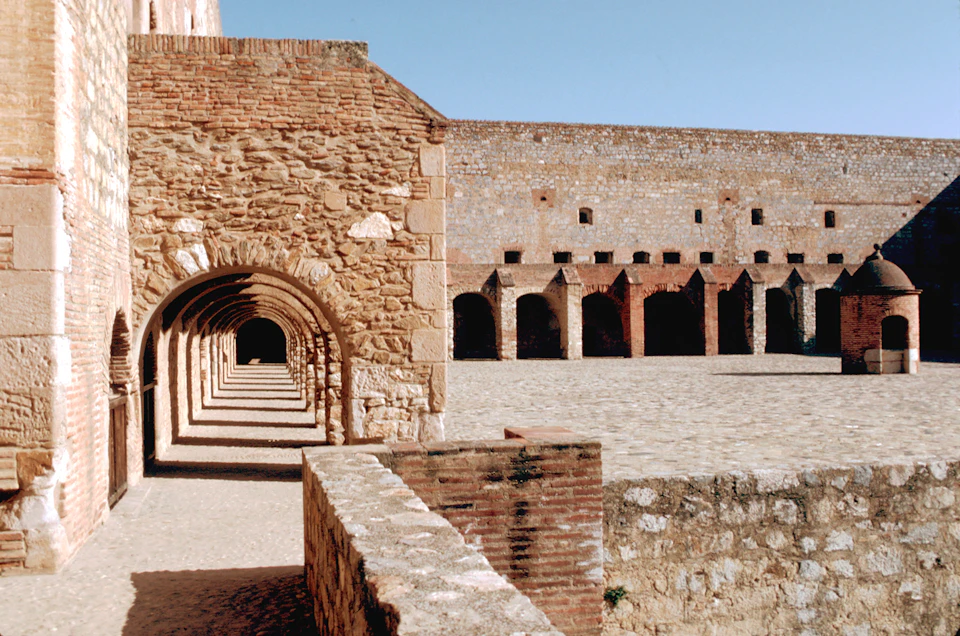 Stone courtyard and archways of an old fortress or historical building under a clear blue sky.