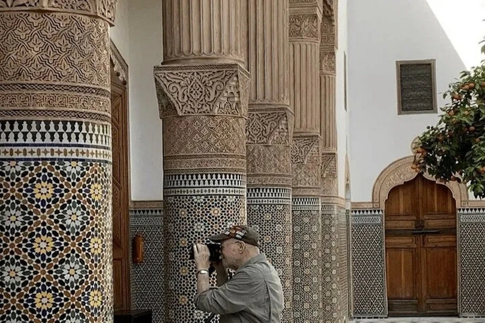 A person with a camera takes pictures of intricately decorated columns in a tiled and ornate building interior.