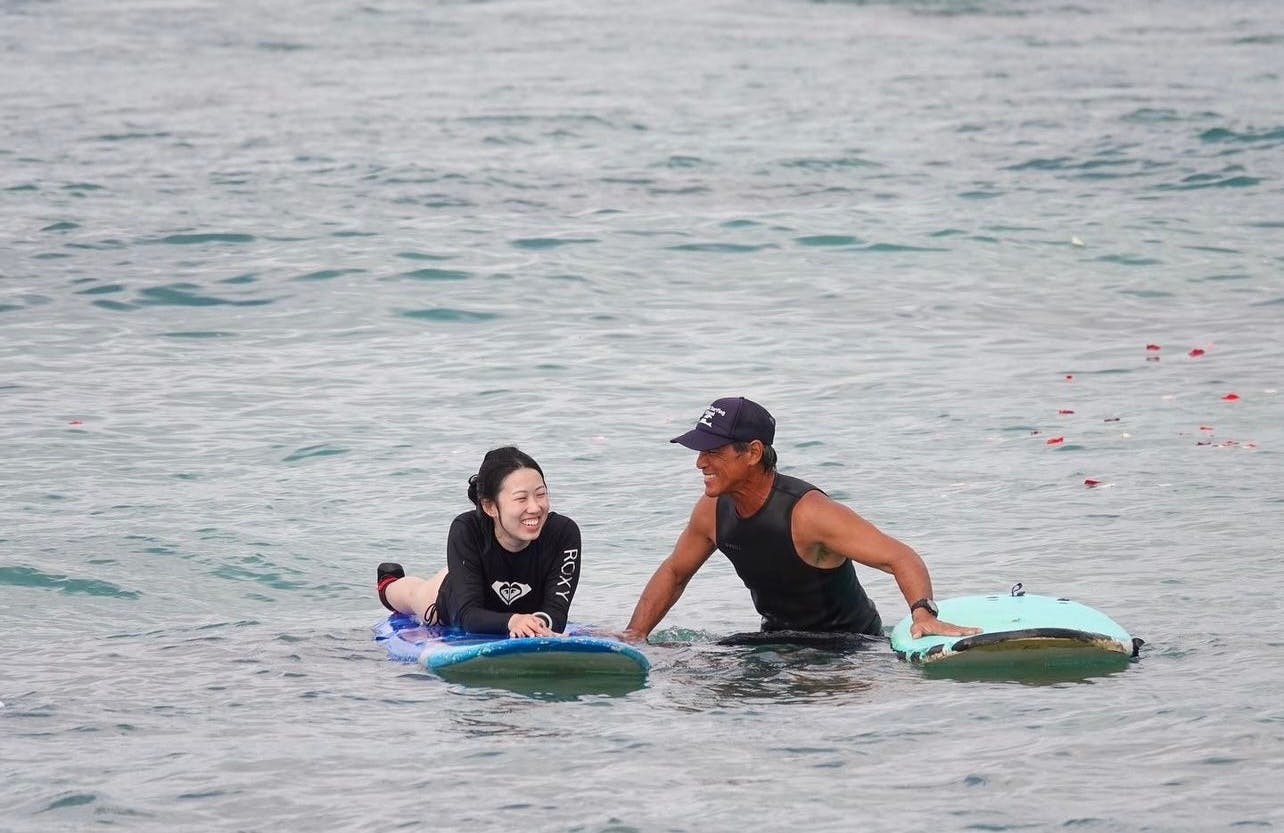 Dues persones en neopres sobre taules de surf flotant sobre aigües tranquil·les, somrient i interactuant.