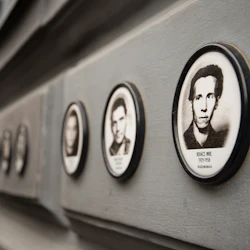 Ovala porträtt av män arrangerade i rad på en grå vägg, var och en med ett namn och datum under fotografiet.