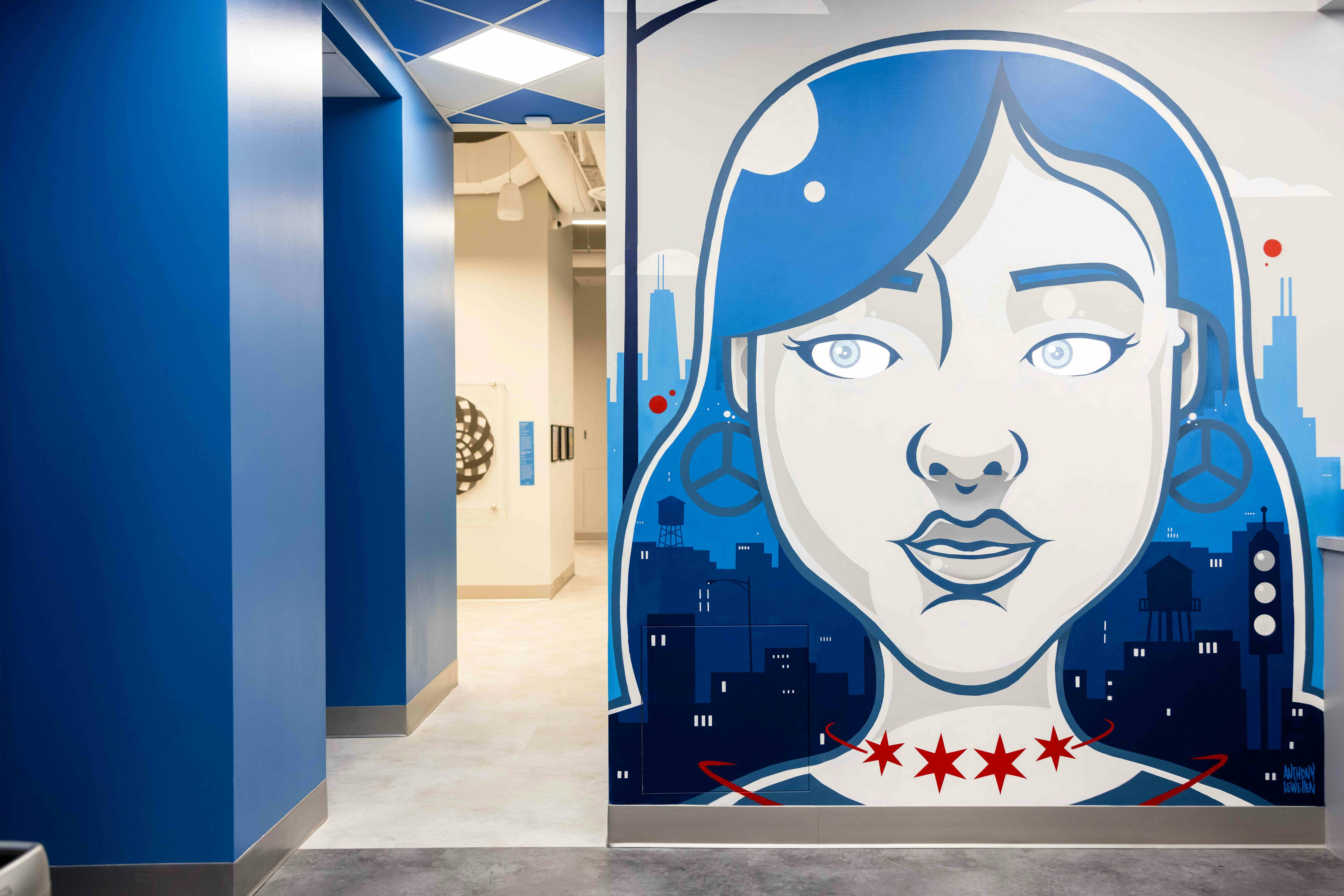 Mural of a stylized woman's face with blue hair, set against a cityscape, featuring the Chicago skyline and red stars at her neck.