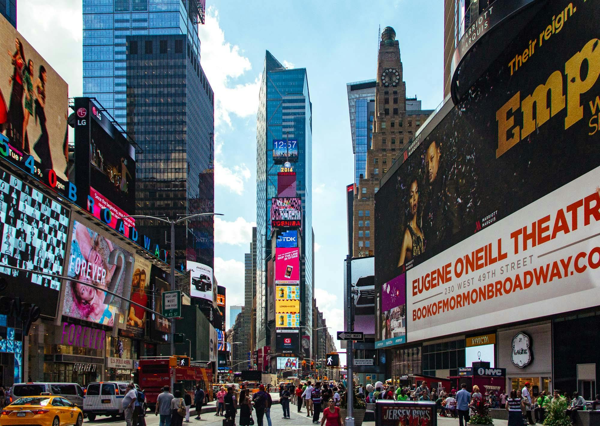 View of Times Square in New York City with large digital billboards, tall buildings, and crowds of people walking.