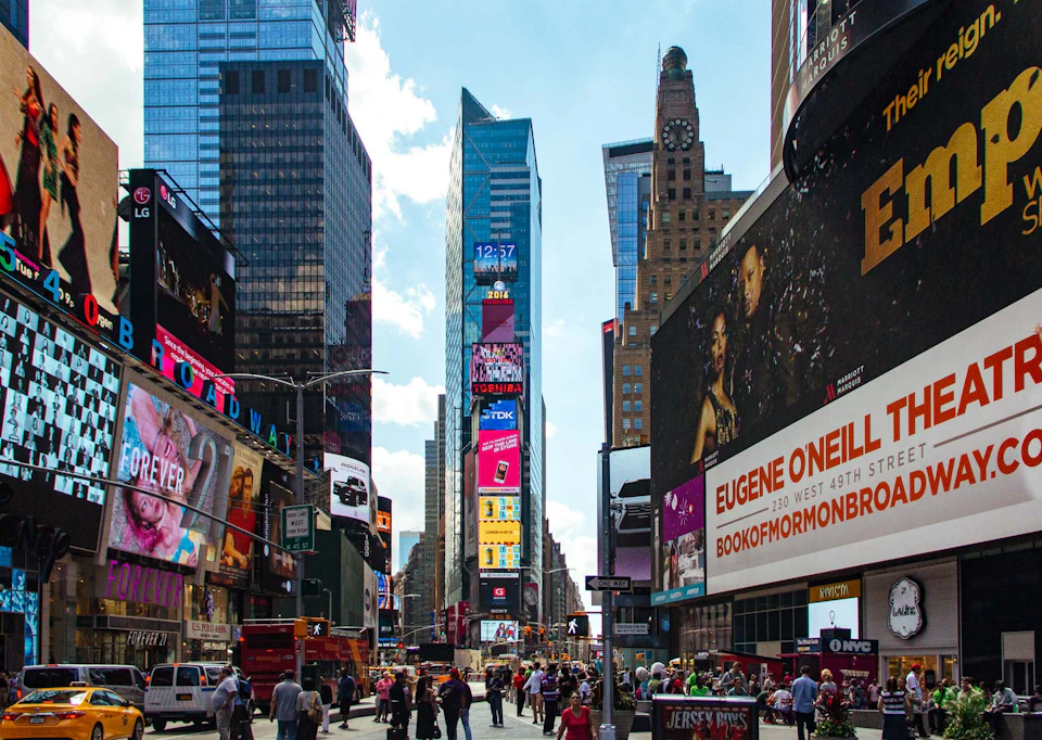 View of Times Square in New York City with large digital billboards, tall buildings, and crowds of people walking.