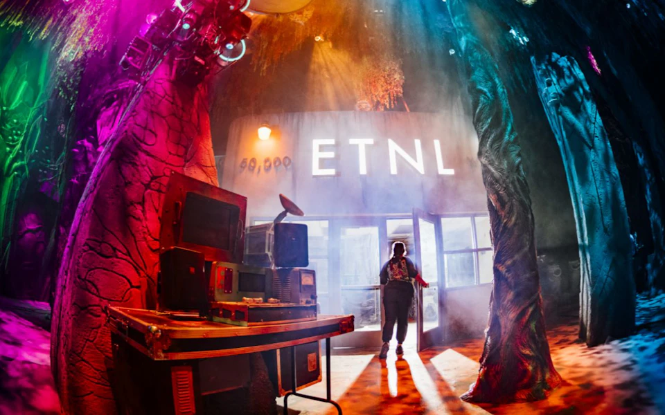 A person stands in front of a building with "ETNL" illuminated on it, surrounded by colorful lights and equipment.