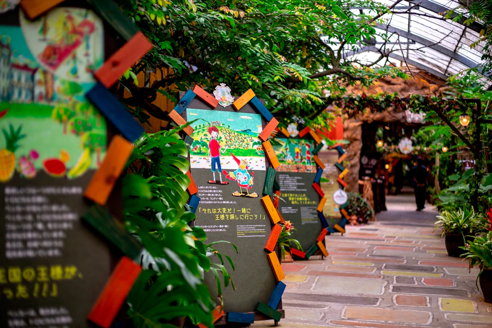 A colorful display with illustrated panels in a greenhouse-like environment, surrounded by plants and a bright pathway.