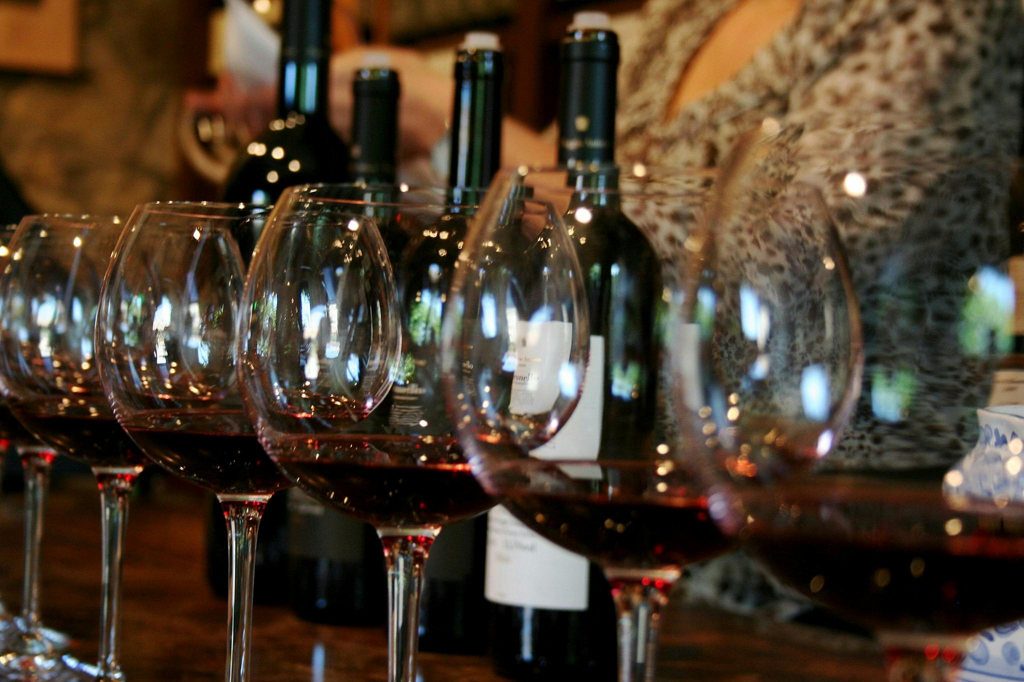 나무 표면에 와인병 몇 개 앞에 레드 와인을 가득 담은 와인잔 네 개를 배경으로 흐릿한 인물이 등장합니다.