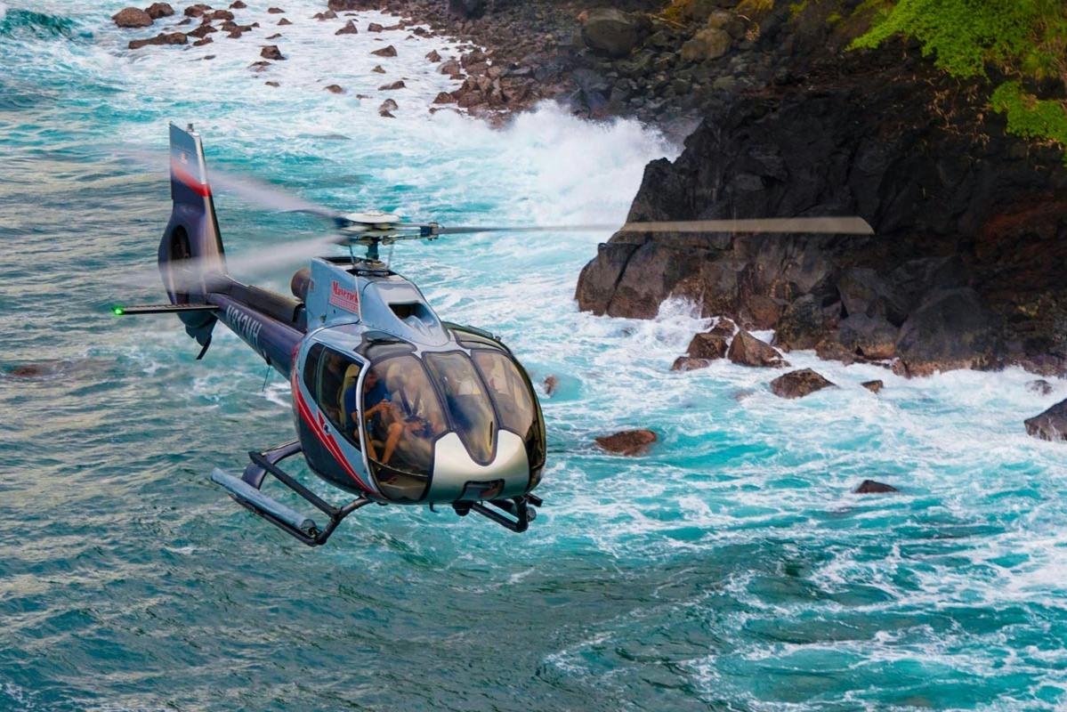 A helicopter flying near rocky ocean cliffs with waves crashing below, showcasing a scenic coastal view.