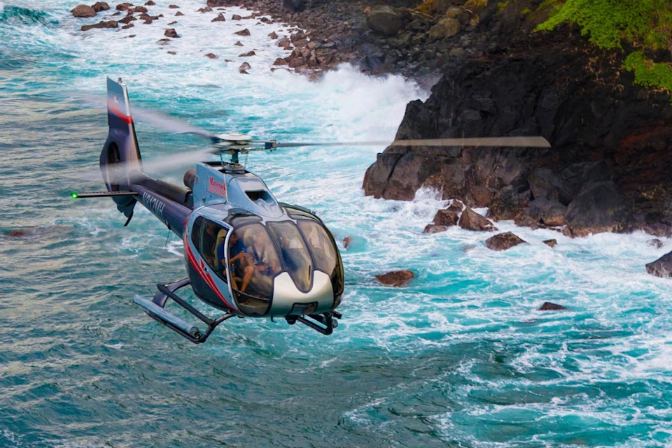A helicopter flying near rocky ocean cliffs with waves crashing below, showcasing a scenic coastal view.