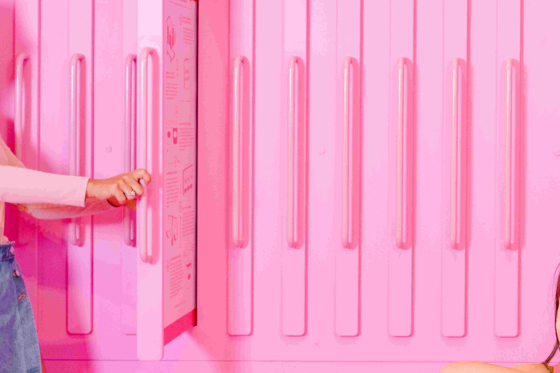 A young girl interacts with objects on a pink counter. A woman opens a cabinet; a man and child stand nearby. All in a pink room.