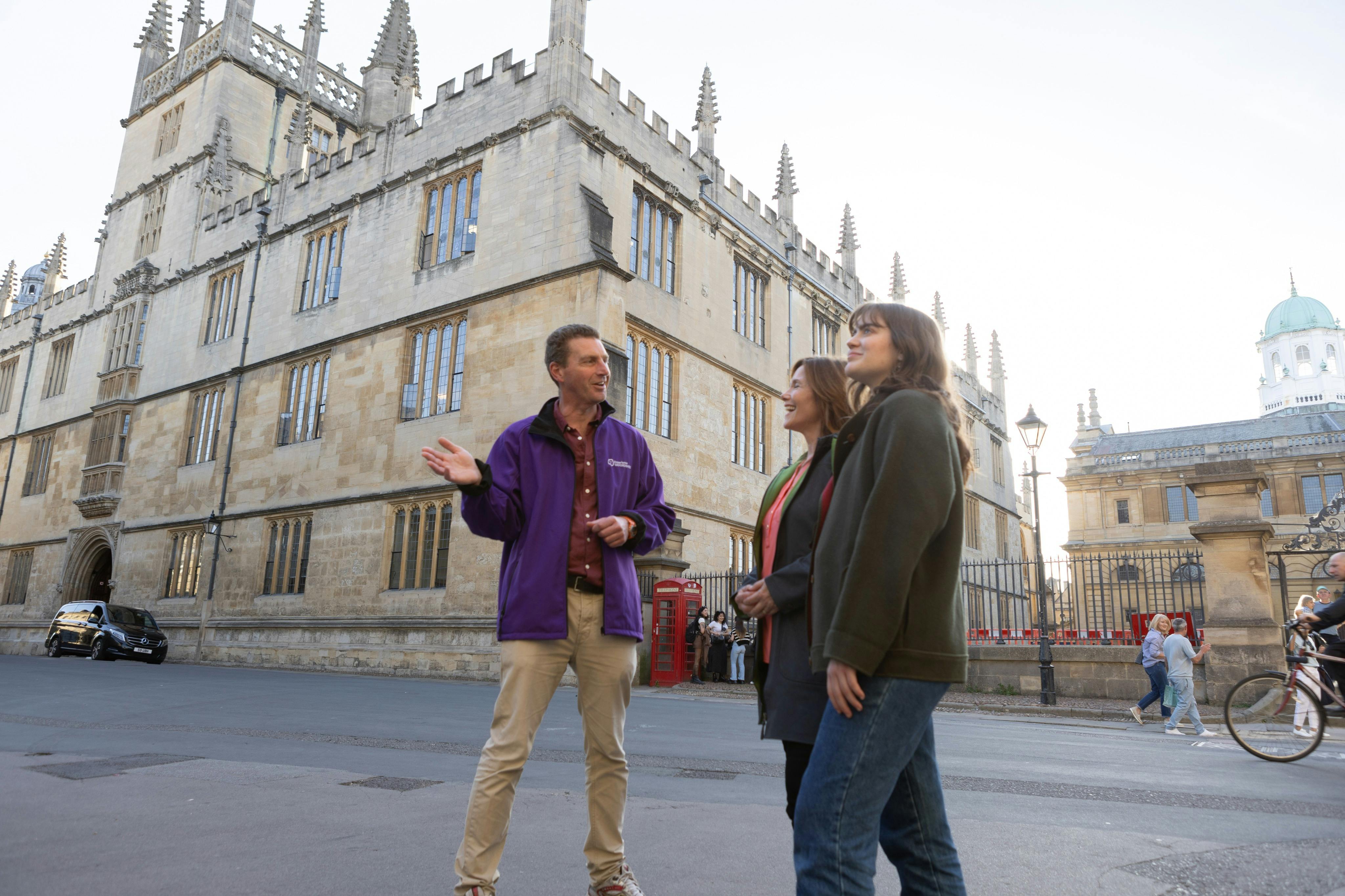 Three people stand talking in front of a historic building with pointed spires, under a clear sky.
