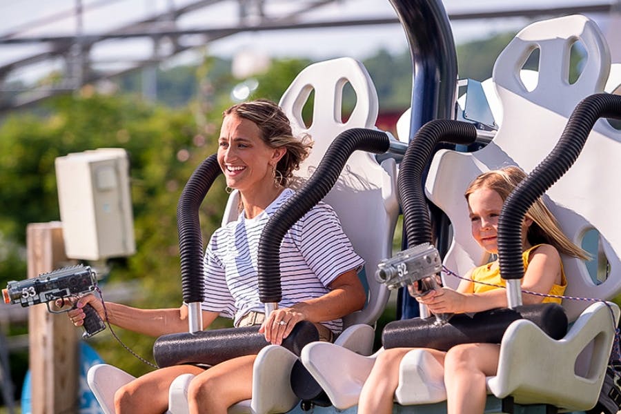 A woman and a child seated on a ride, smiling and enjoying the experience. The child is holding a toy blaster.