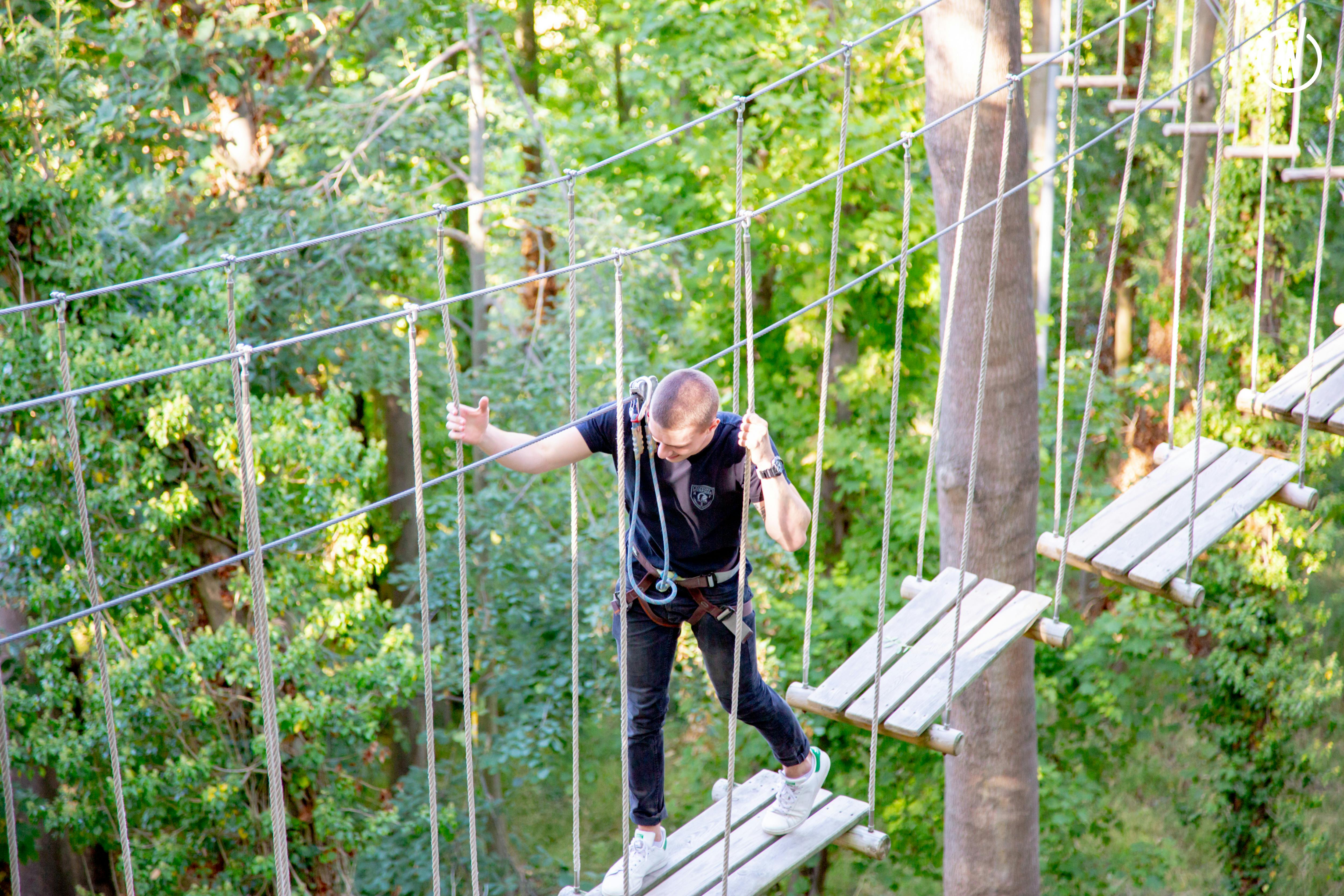 A person in safety gear navigates a rope bridge high among trees in a forest.