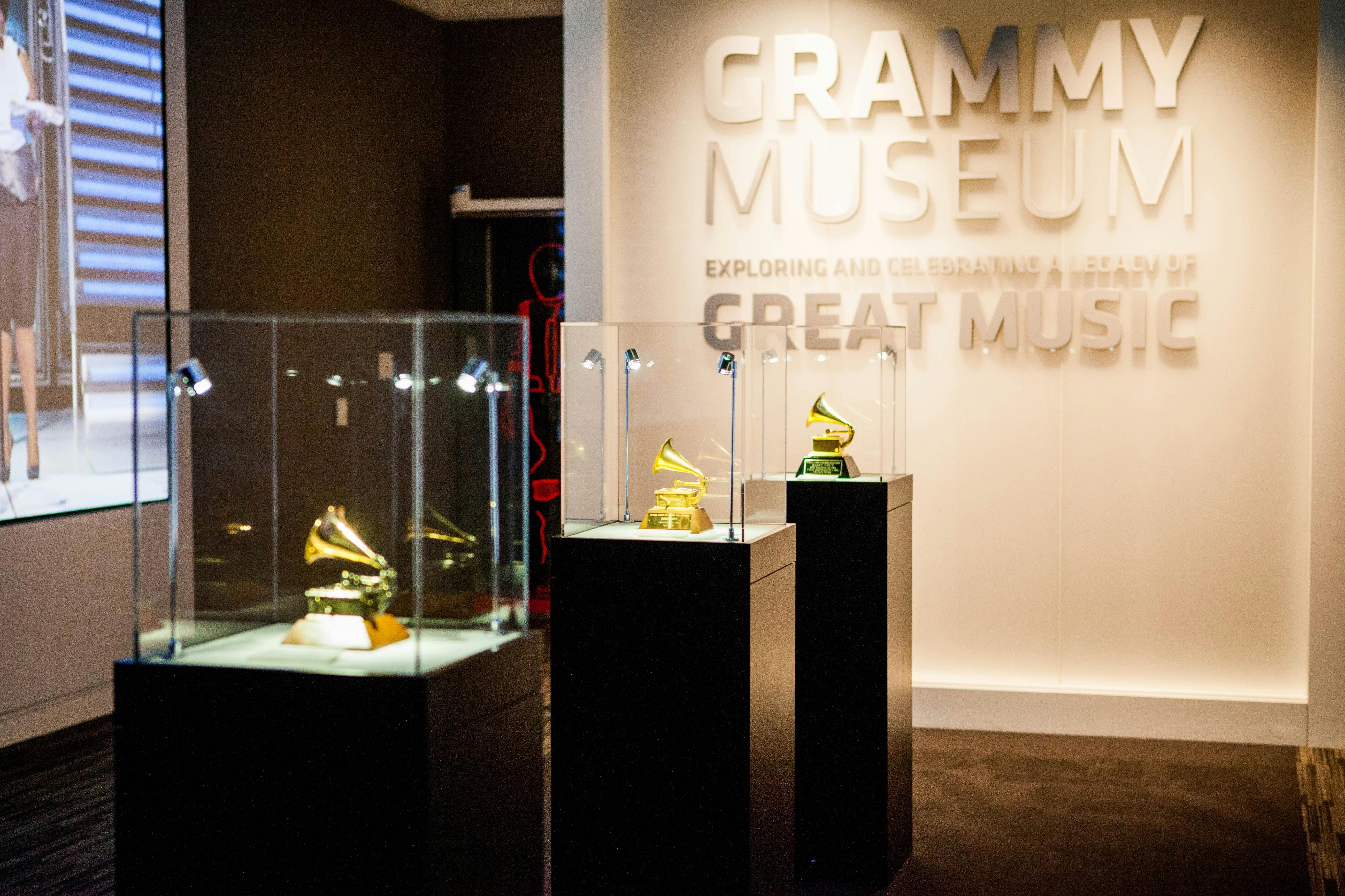 A display of Grammy trophies in glass cases at a museum with a sign on the wall reading "GRAMMY Museum."