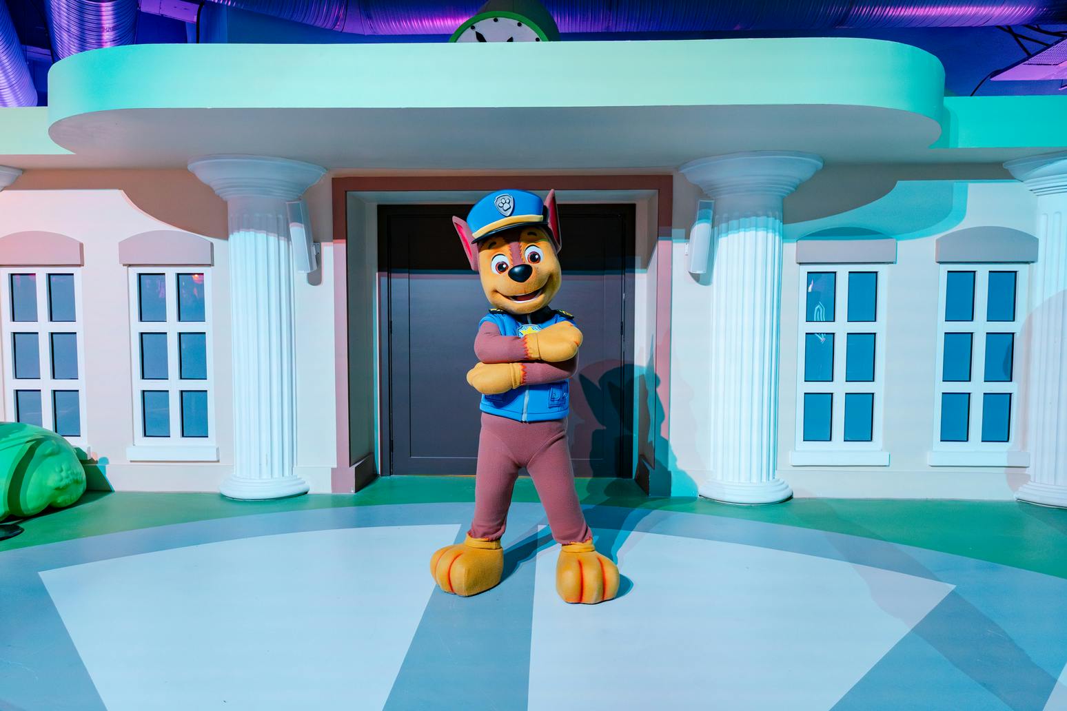 Een gekostumeerd personage dat op een hond lijkt staat zelfverzekerd voor een gebouw met zuilen en grote ramen.