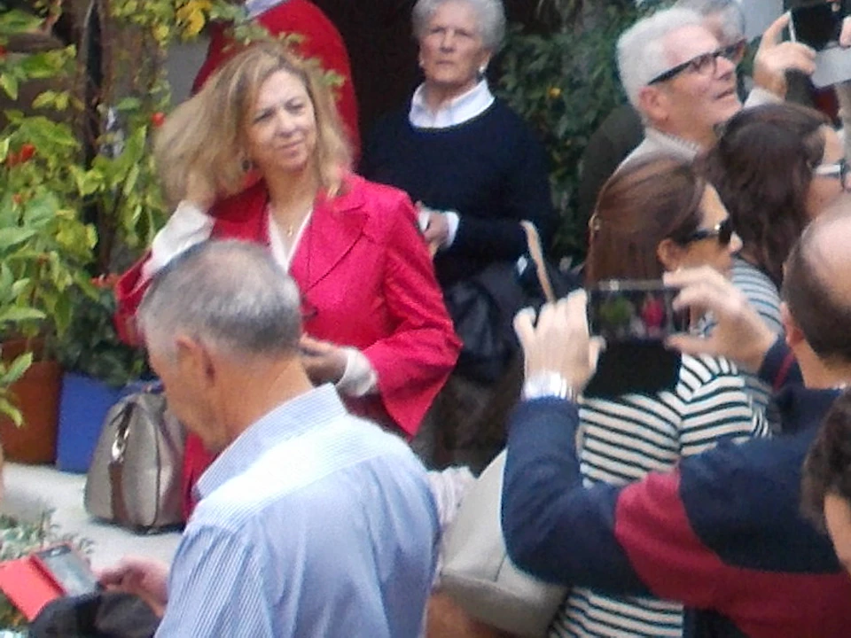 A group of people in a courtyard adorned with many potted plants and flowers on walls, with lanterns and a tiled-roof building.