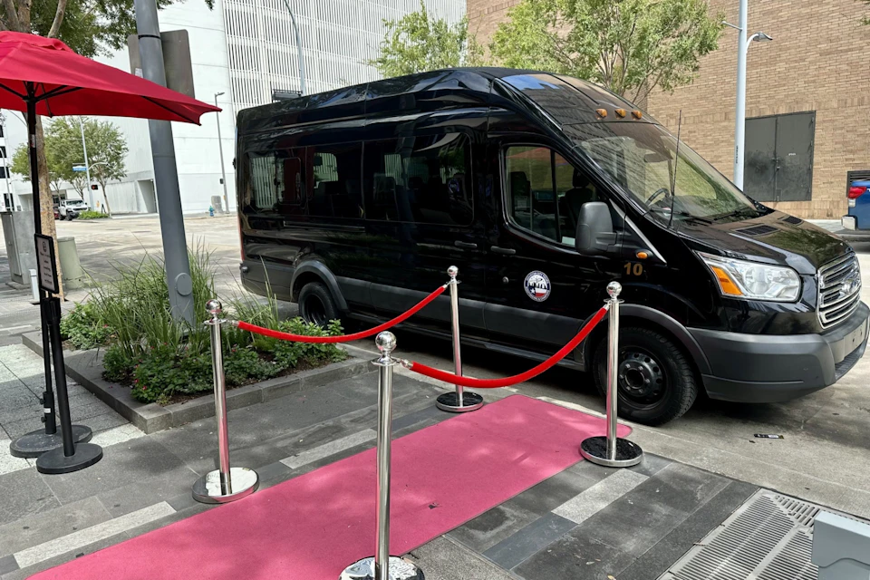 A black van is parked on a city street behind a red carpet setup with stanchions and red ropes.