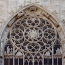 Intricate Gothic-style rose window with ornate stone carvings and statues, set in an arched frame on a stone building facade.
