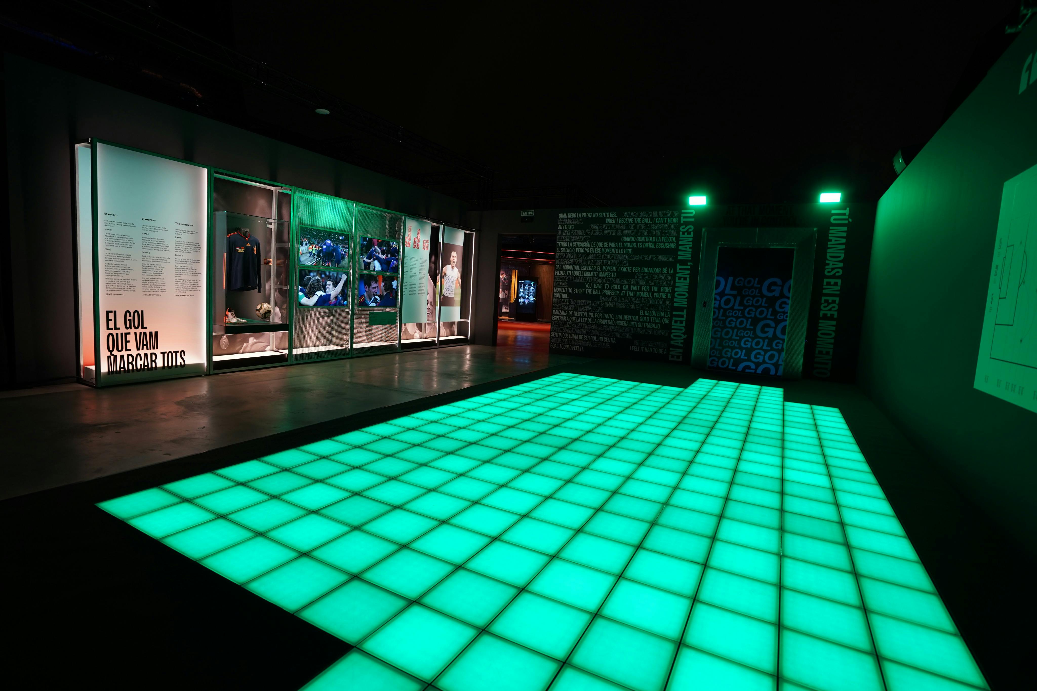 An illuminated green tiled floor in a modern exhibit space with display cases and wall texts around it.