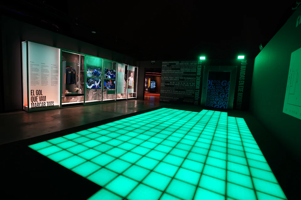 An illuminated green tiled floor in a modern exhibit space with display cases and wall texts around it.
