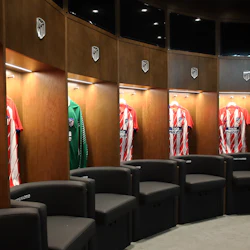 Ett omklädningsrum med Atlético Madrid-tröjor som visas i träskåp ovanför svarta stolar.