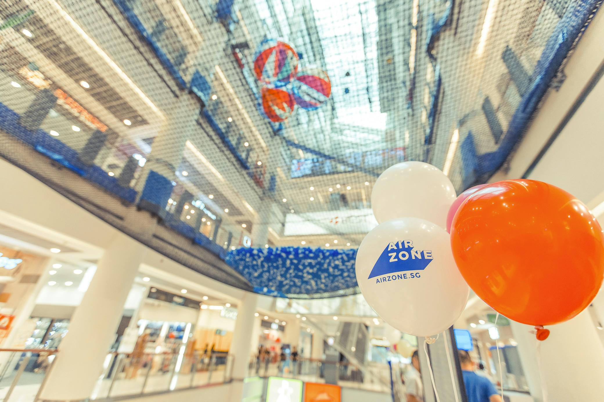 Centro commerciale con area giochi in rete sospesa sopra, con palloncini colorati con la scritta "AIRZONE".