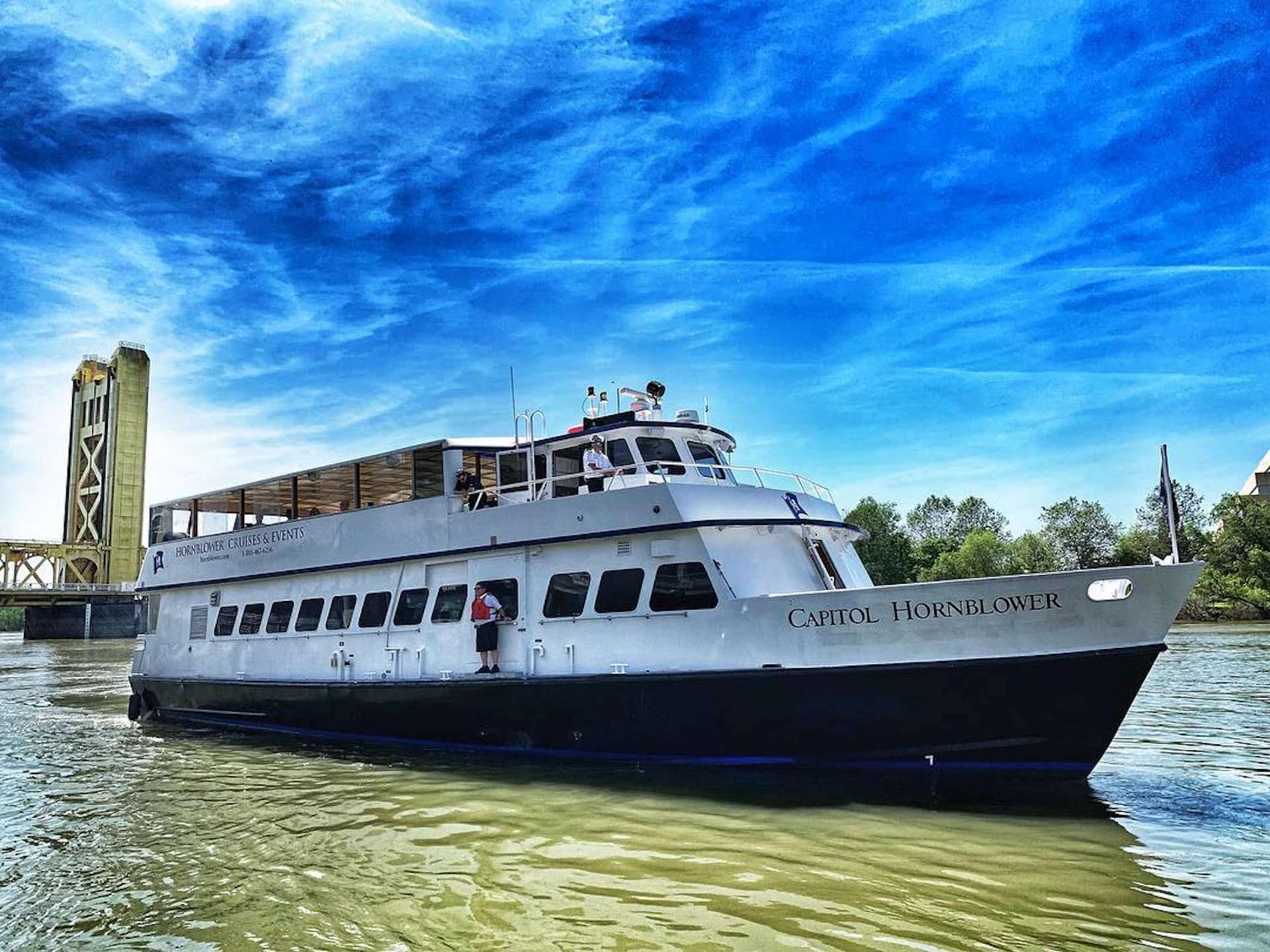 A white boat named "Capitol Hornblower" on water with a clear blue sky and trees in the background.