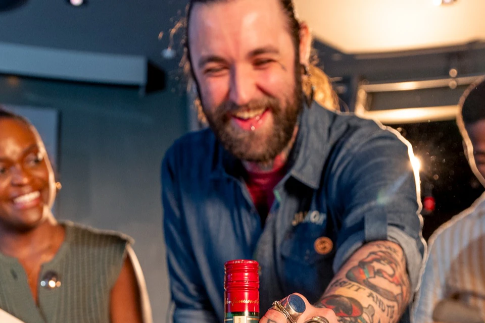 A group of people smiling around a table with a bottle of Jameson Irish Whiskey in the foreground.