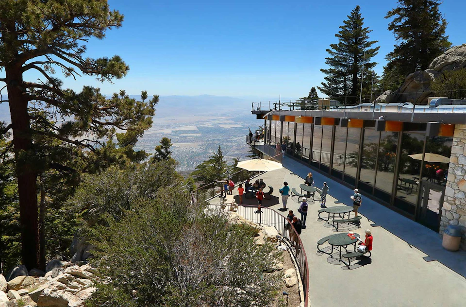 People enjoying the view on a spacious terrace with tables and umbrellas near a building, overlooking a vast landscape.