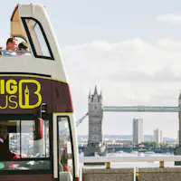 Autocarro turístico de dois andares com o logótipo "BIG BUS", pessoas no andar superior, a Tower Bridge ao fundo sob um céu parcialmente nublado.