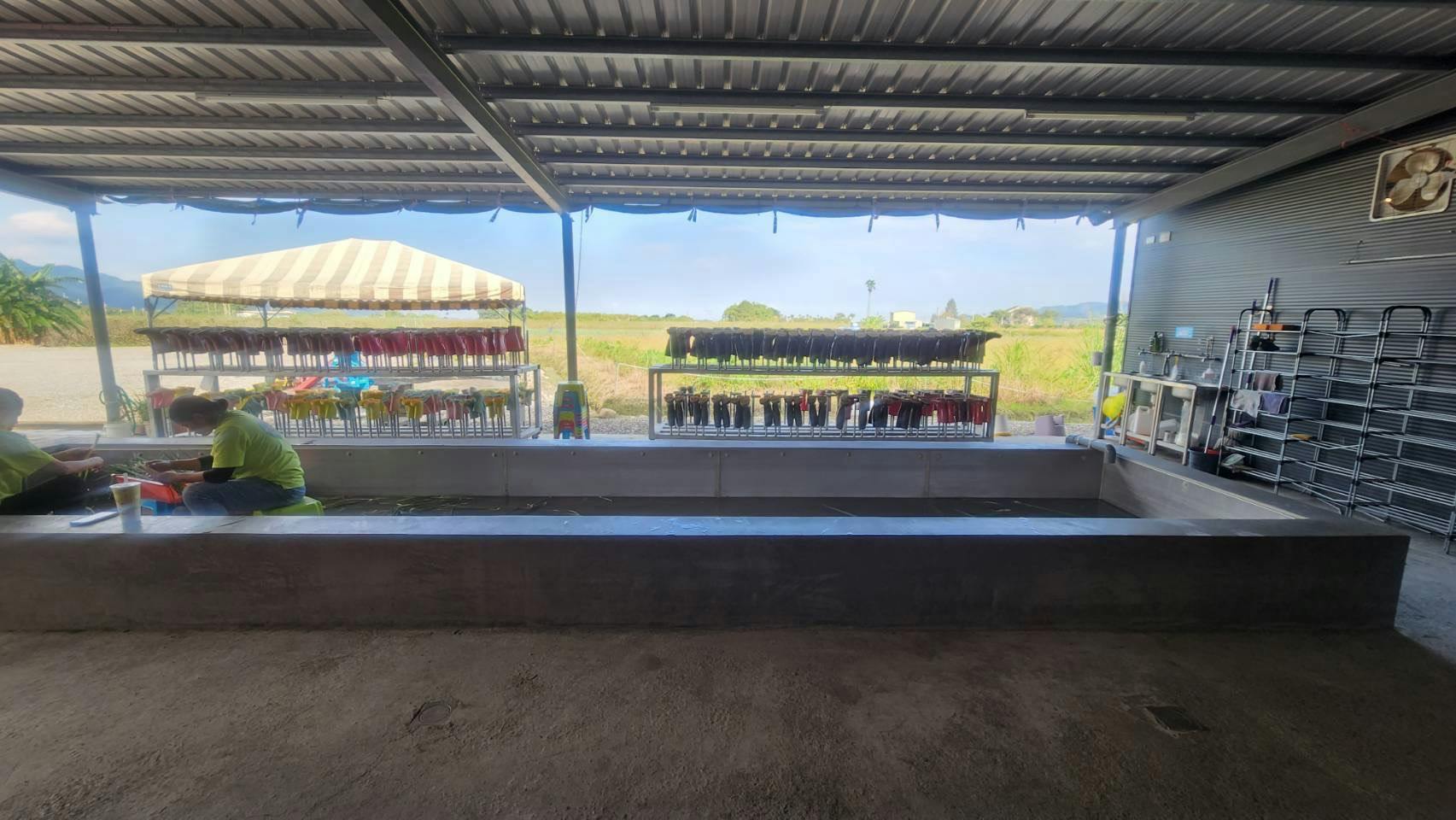 A sheltered outdoor area with racks of drying items, possibly umbrellas, and a view of a field and mountains beyond.