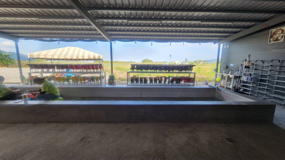 Rows of colorful items displayed on racks under a metal roof, with an open field and blue sky visible in the background.