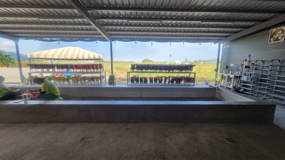 Rows of colorful items displayed on racks under a metal roof, with an open field and blue sky visible in the background.