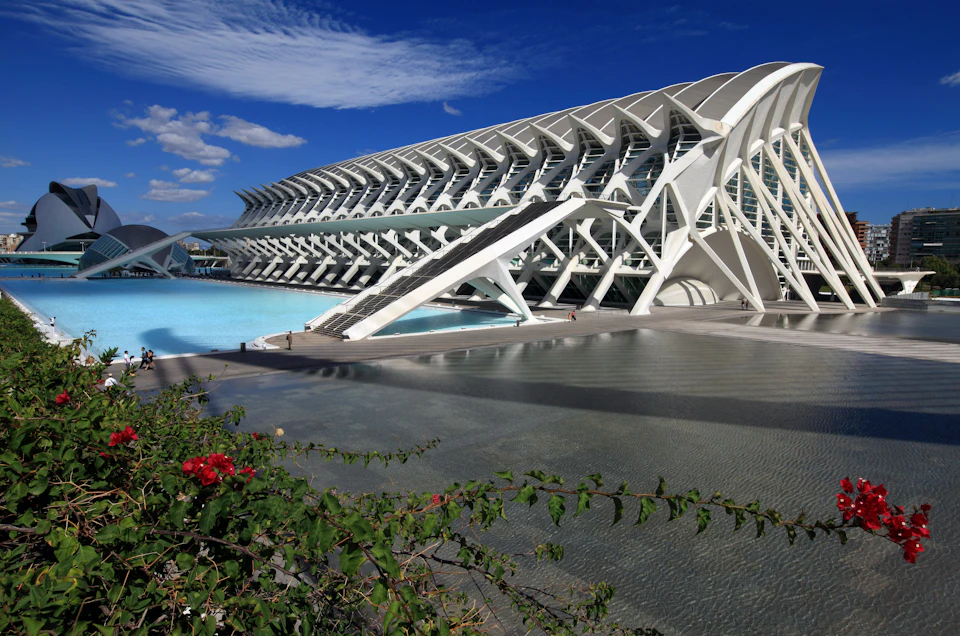Futuristic white architecture with curved designs, set against a blue sky. Reflecting pools and greenery in the foreground.
