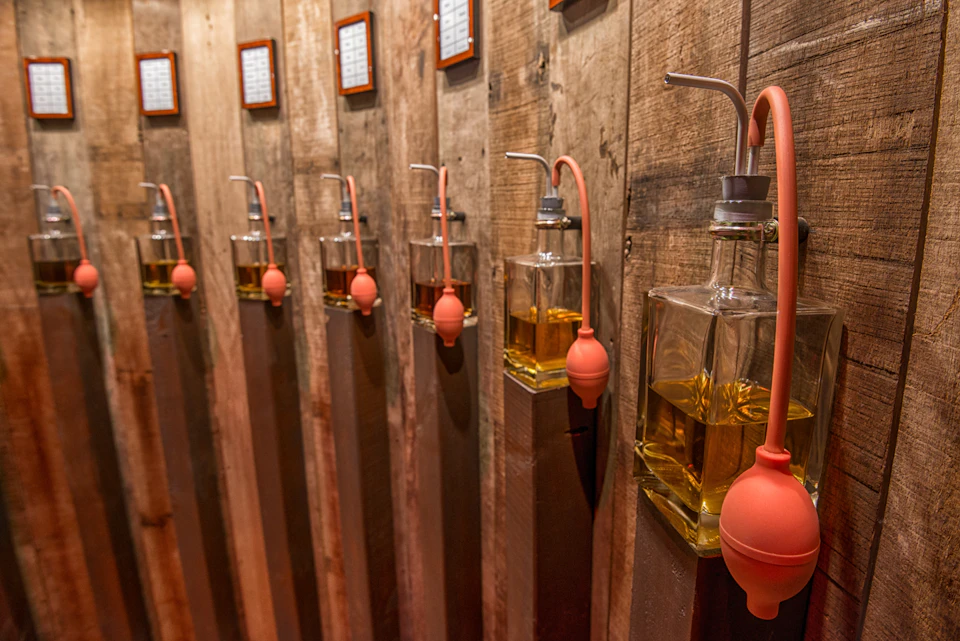Rows of glass dispensers with orange bulbs, each filled with amber liquid, mounted on rustic wooden wall panels.