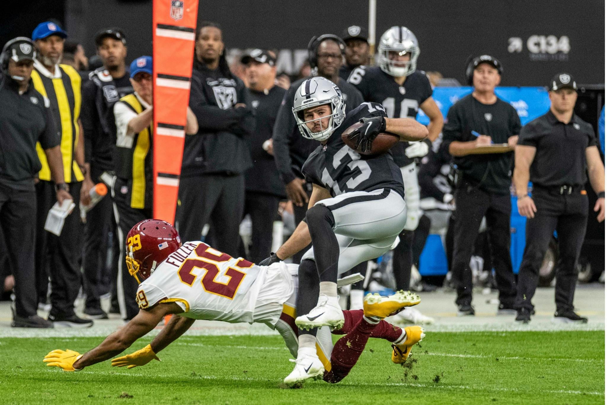 A football player in a black uniform is tackled by an opponent in white and burgundy during a game on a grass field.