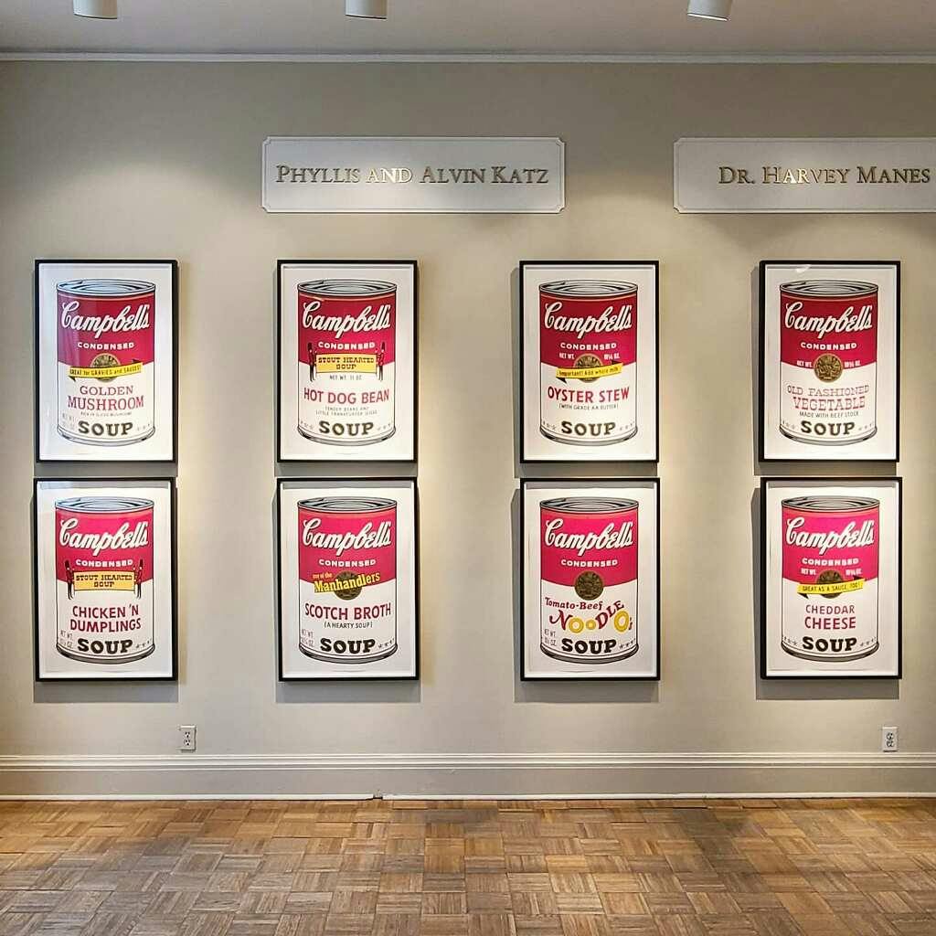 Seks indrammede Campbells suppe kan prints hænge på en gallerivæg med navnene "Phyllis og Alvin Katz" og "Dr. Harvey Manes" ovenfor.