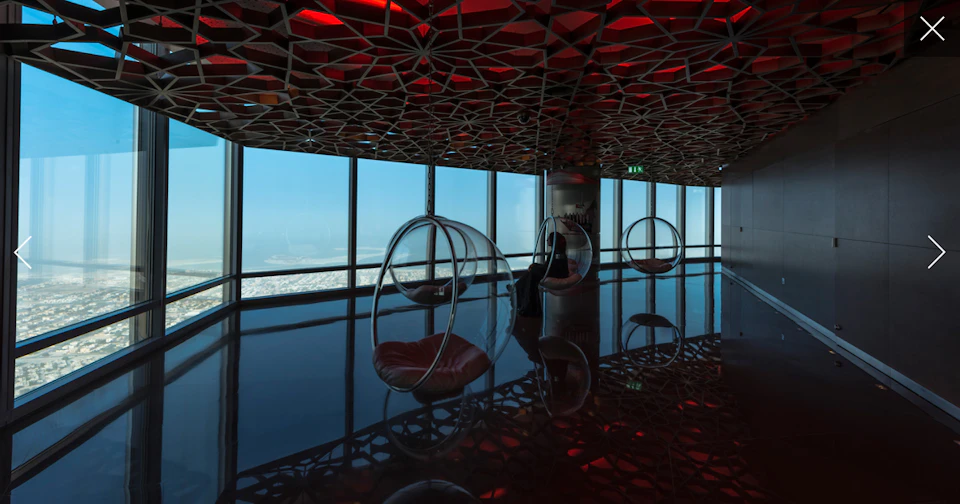 Modern lounge with hanging bubble chairs against floor-to-ceiling windows, intricate ceiling, and panoramic ocean view.