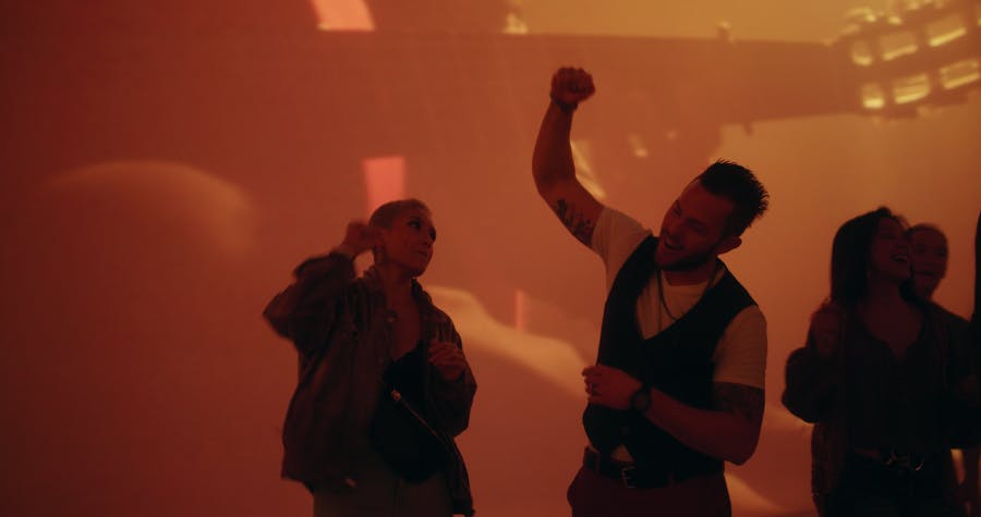 暖かいオレンジ色に照らされた背景に向かって、拳を上げた2人の人物が笑顔で踊っています。