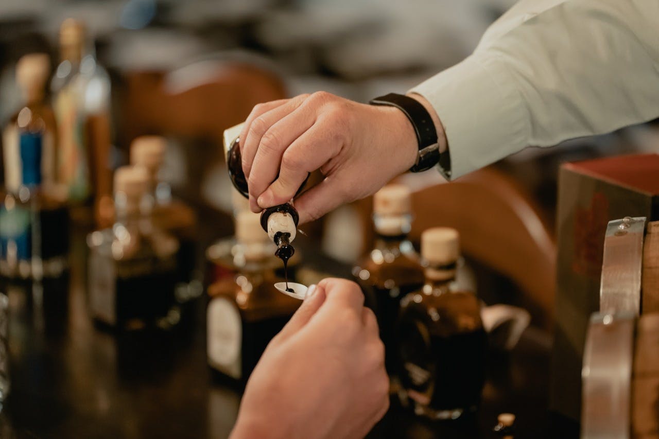 小さなボトルから別の人が持っているスプーンに液体を注ぎます。背景には数本のボトルが見えます。