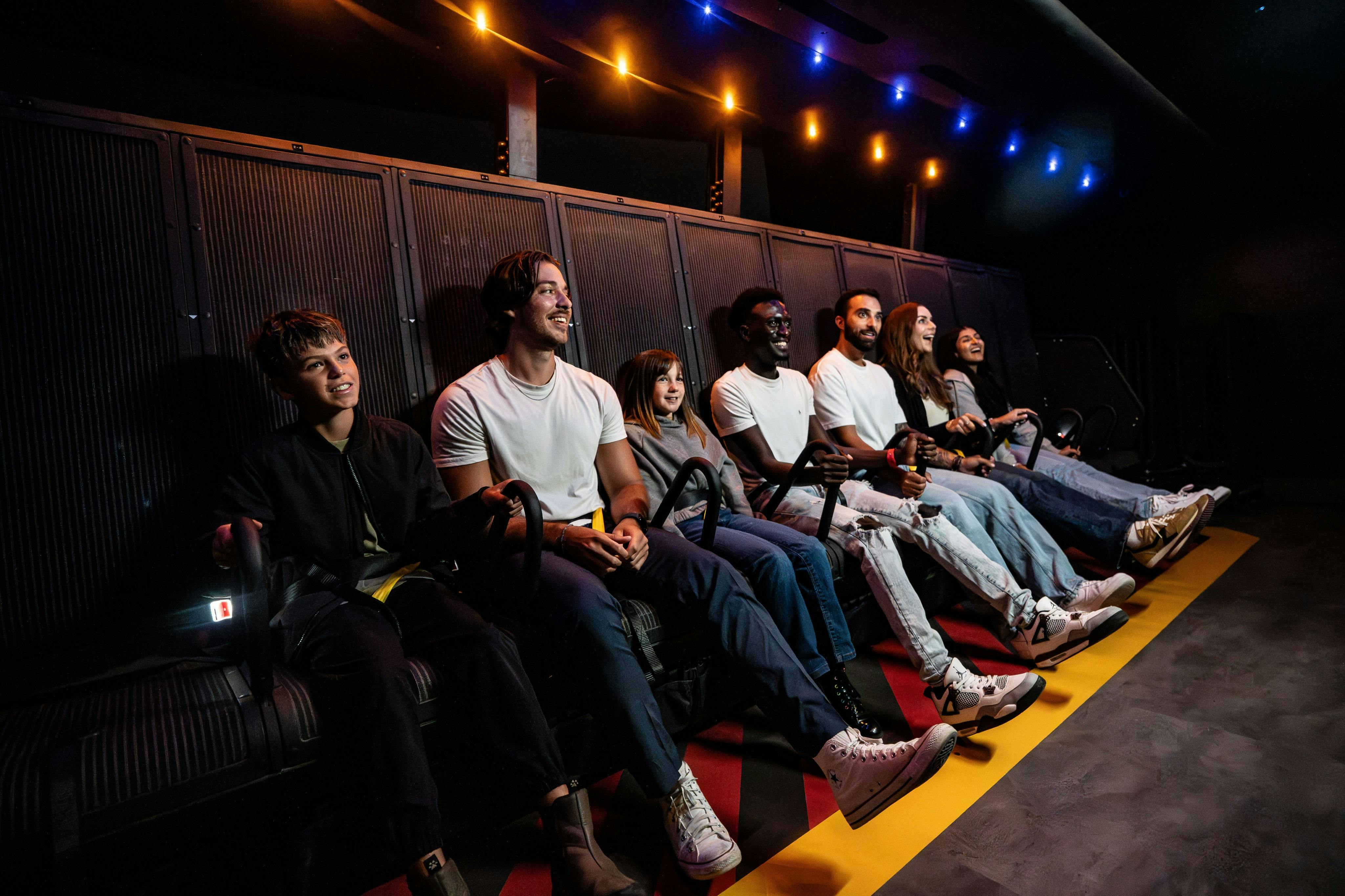 一群戴着3D眼镜的人坐在运动模拟器上，在五颜六色的灯光下看起来很兴奋。