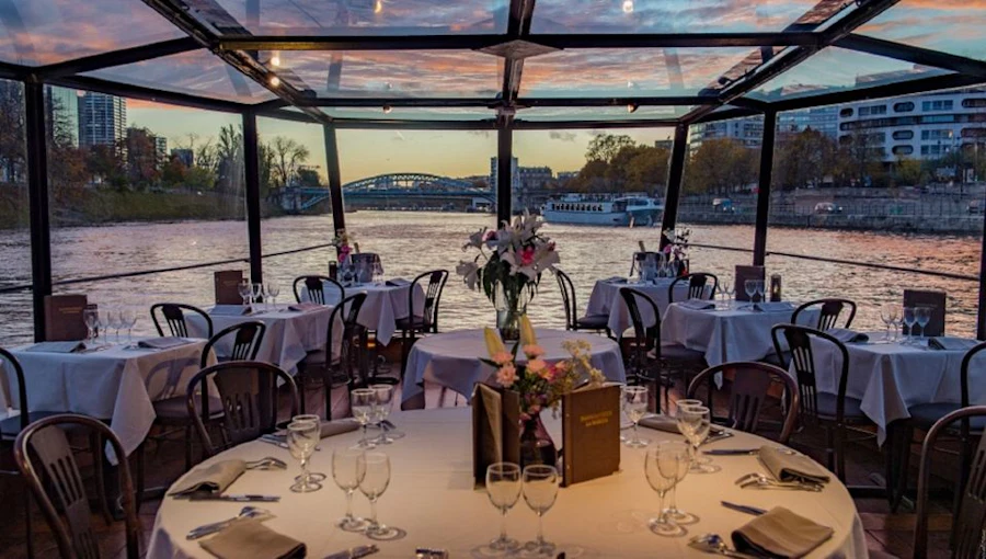 Elegantly set tables on a glass-roofed boat at sunset overlooking the Seine